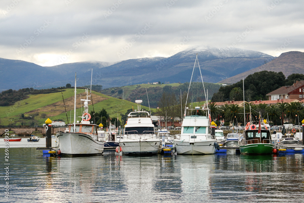 Pleasure boats moored in a harbor with a mountain background with snow and cloudy sky