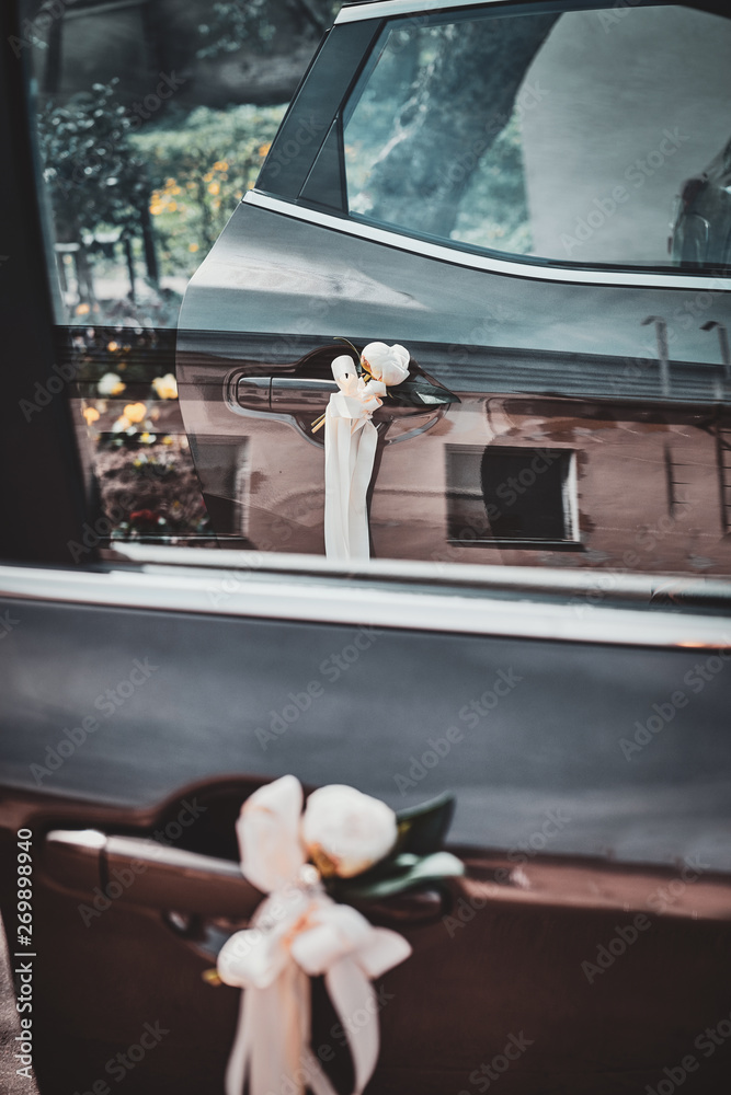 Festive car decorated with white roses and bows on the door handles.