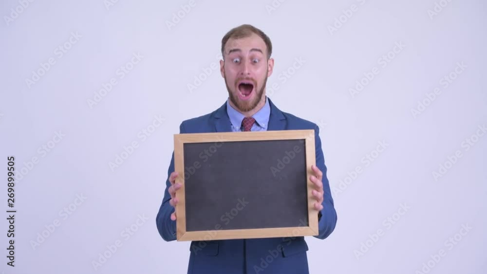 Happy bearded businessman holding blackboard and looking surprised