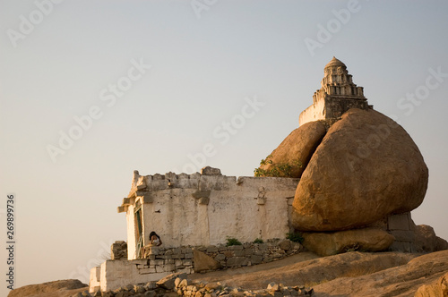 A man sits at a stone Hindu unique temple of Shiva in Hampi, India at dawn.