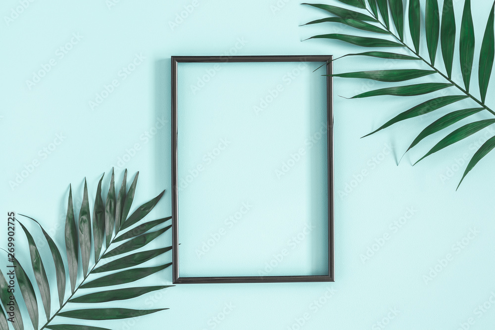 Summer composition. Tropical palm leaves, black photo frame on pastel blue background. Summer, nature concept. Flat lay, top view, copy space - obrazy, fototapety, plakaty 
