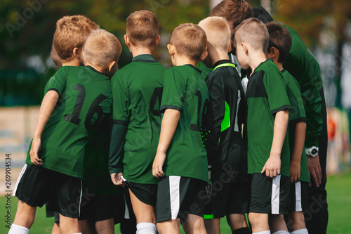 Fototapeta Naklejka Na Ścianę i Meble -  Group of Young Boys in Green Jersey Shirts Standing with Coach on Soccer Field. Sports Team Putting Their Hands in Together. Pre-game Coach Speech. Junior Kids Sports Team with Coach