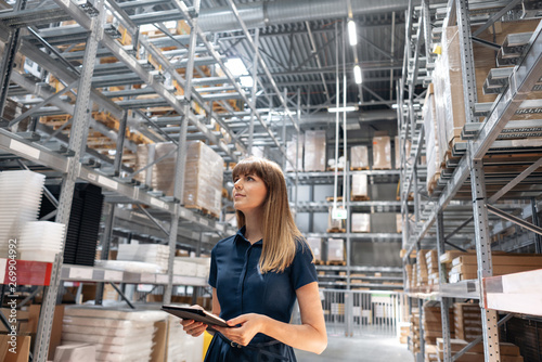 Wholesale warehouse. Beautiful young woman worker of store in shopping center. Girl looking for goods with a tablet is checking inventory levels in a warehouse. Logistics concept