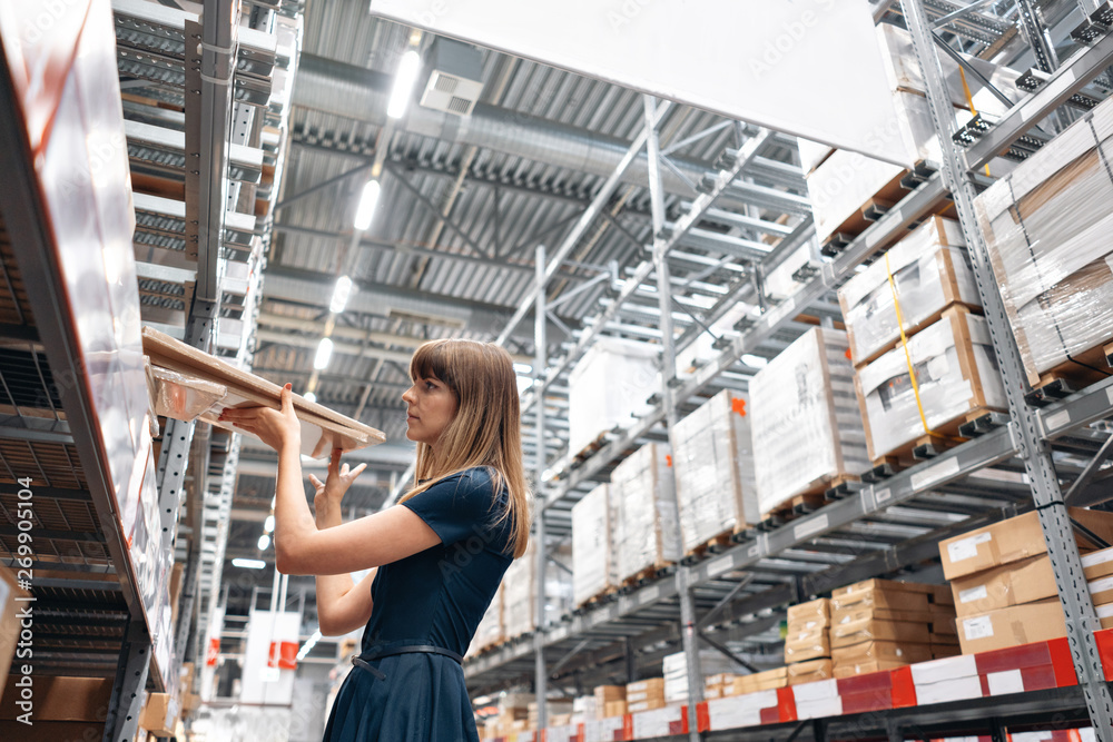 Fototapeta premium Wholesale warehouse. Beautiful young woman worker of store in shopping center. Girl looking for goods with a tablet is checking inventory levels in a warehouse. Logistics concept