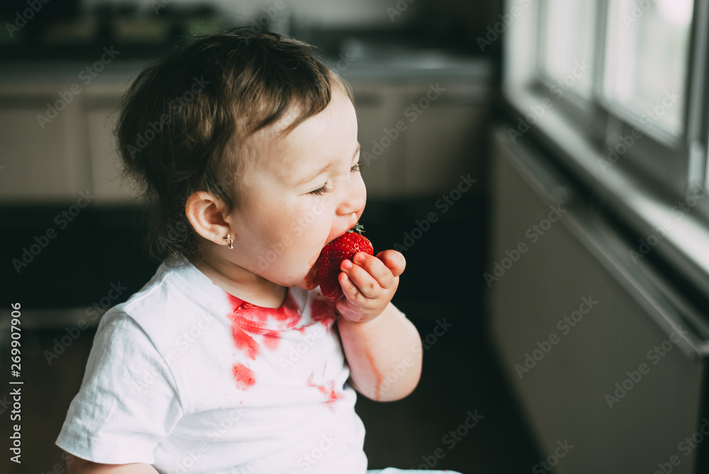 A little girl in a white t-shirt all dirty climbed on the table sitting and eating strawberries A little girl in a white t-shirt all dirty climbed on the table sitting and eating strawberries