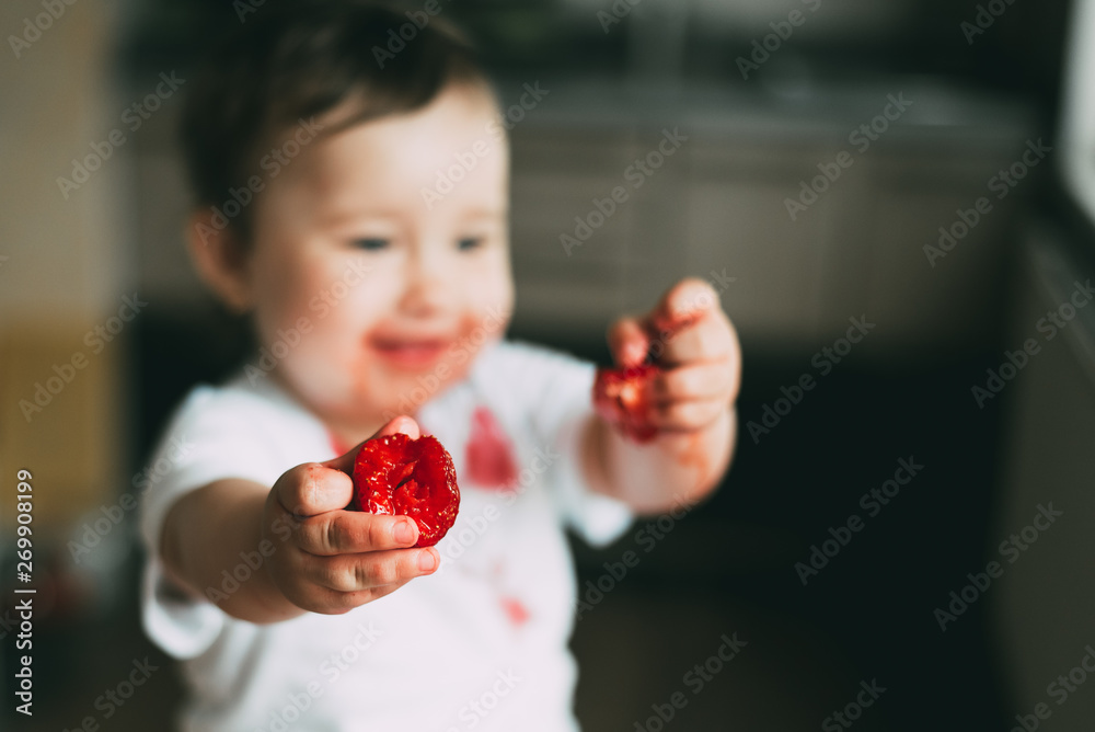 A little girl in a white t-shirt all dirty climbed on the table sitting and eating strawberries A little girl in a white t-shirt all dirty climbed on the table sitting and eating strawberries