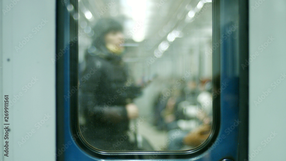 Blurred background people in the underground carriage. Passenger sitting in underground train, view through glass door. Modern city transport.