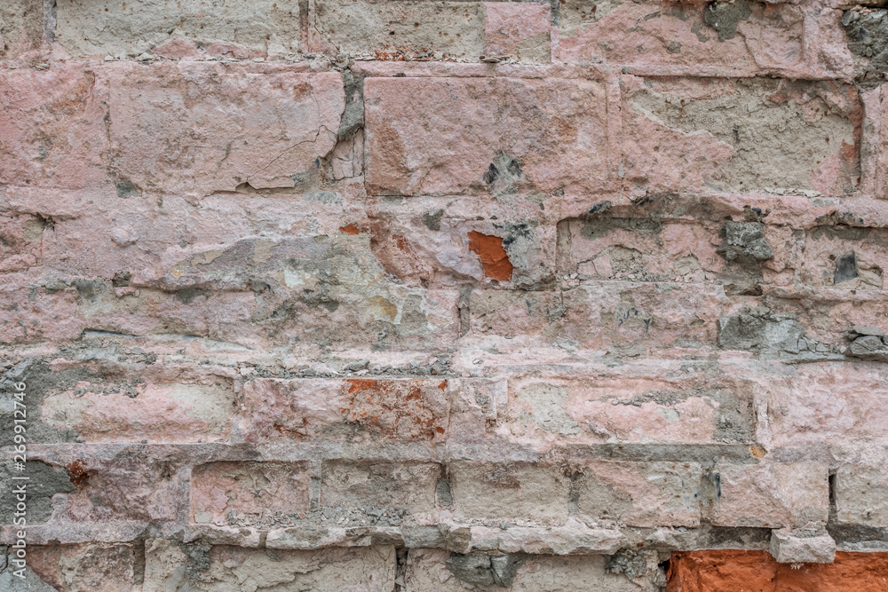 abstract background of an old brick wall with peeling plaster and the remains of pink paint close up