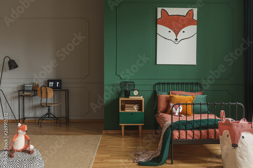 Real photo of a fox painting hanging on a green wall with molding, above black, metal bed in a kid's room interior photo