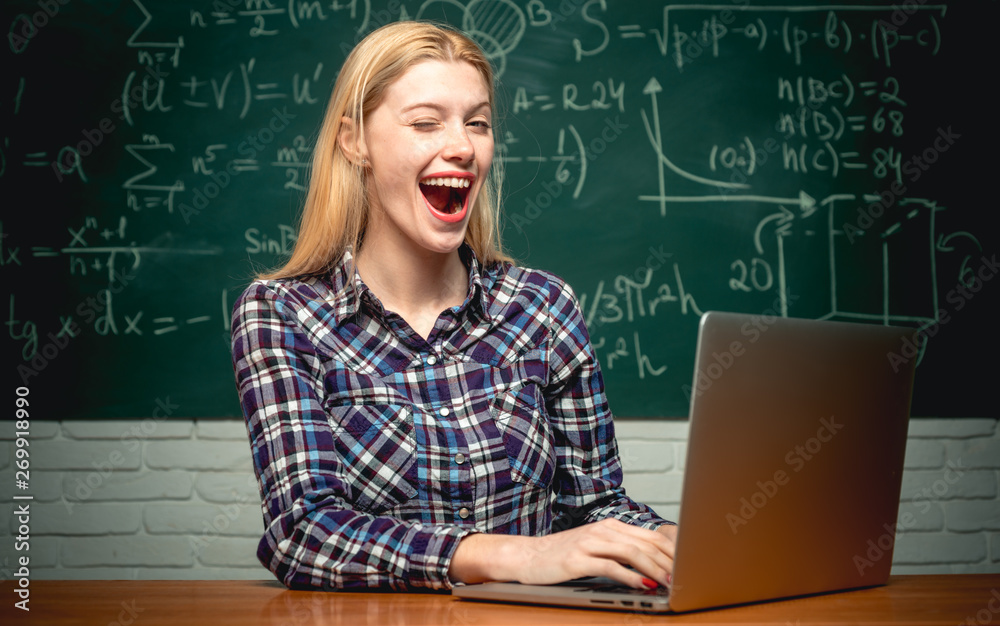 Female student looking at camera. Cheerful smiling girl student at the blackboard. College tutor. Student sitting at table and writing on notebook Female student looking at camera. Cheerful smiling girl student at the blackboard. College tutor. Student sitting at table and writing on notebook