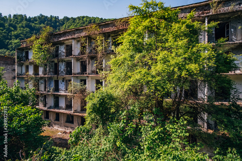 Ruined overgrown apartment house in ghost mining town, consequences of war in Abkhazia, green post-apocalyptic concept © Mulderphoto