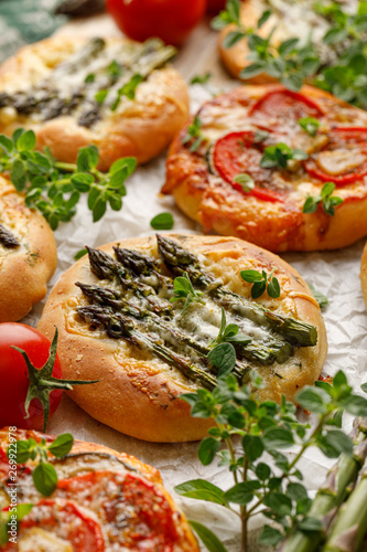 Mini pizzas with the addition of green asparagus, tomatoes, cheese and herbs, close-up. Vegetarian pizzas, delicious appetizer