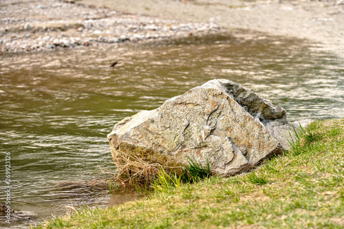 Large boulder rock on grass side of the river.
