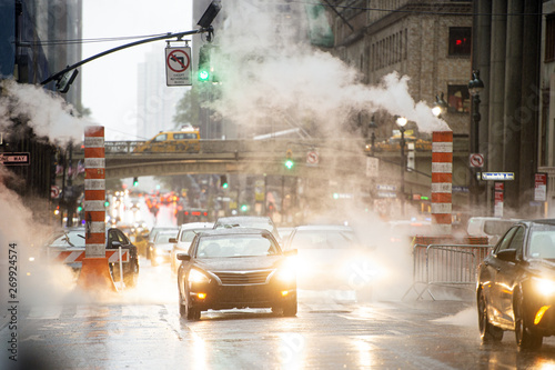 Some cars are crossing the 42nd street in Manhattan while steam coming out from from the manholes. New York City, Usa. 42nd Street is a major crosstown street in Manhattan.