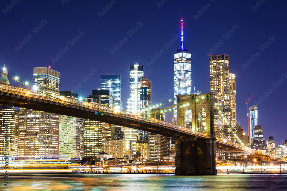 Stunning view of the Brooklyn Bridge and the illuminated Manhattan's skyline at dusk with dark blue sky and smooth water surface. Picture taken from the Brooklyn district, New York, USA.