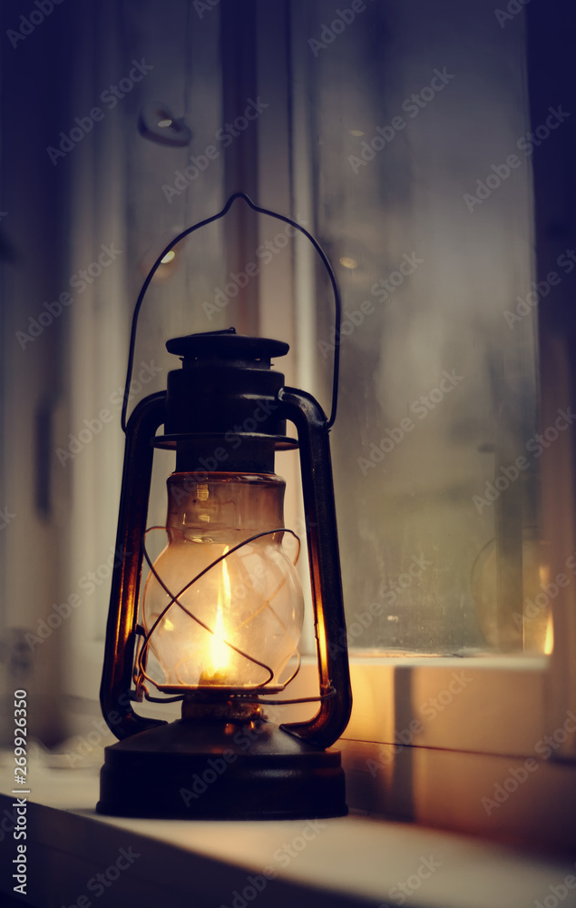 An old kerosene lamp stands on a white windowsill