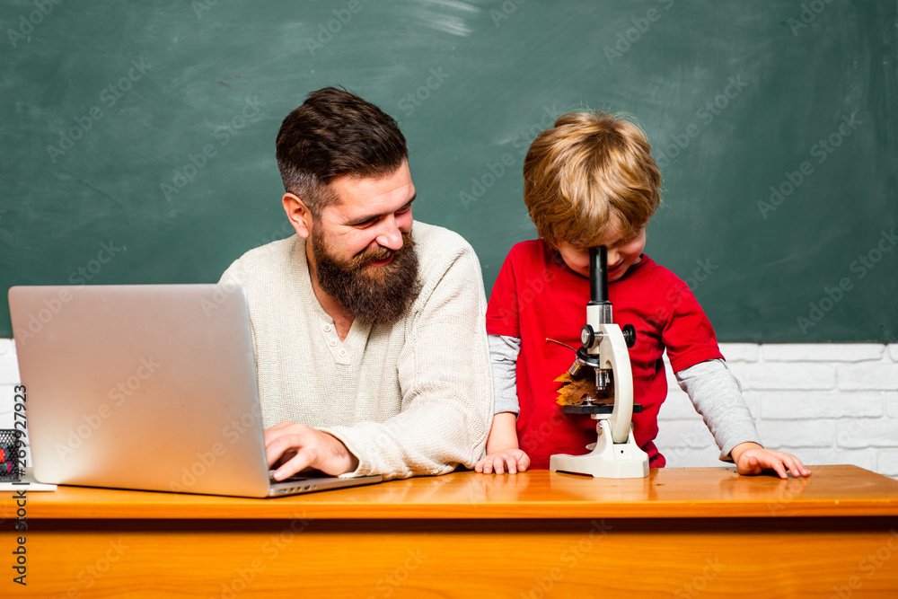 Elementary school teacher and student in classroom. Daddy play with schoolboy. Teacher and schoolboy using laptop in class. Teacher helping pupils studying on desks in classroom.