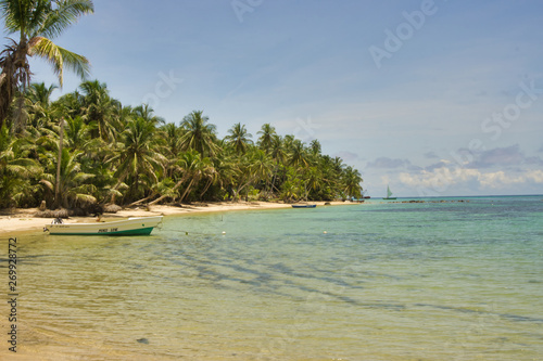 photo island landscape full of coconut palms with fishing boats, crystal clear water and a blue sky