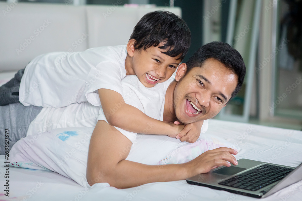 Happy man and his son using a laptop on bed Happy man and his son using a laptop on bed