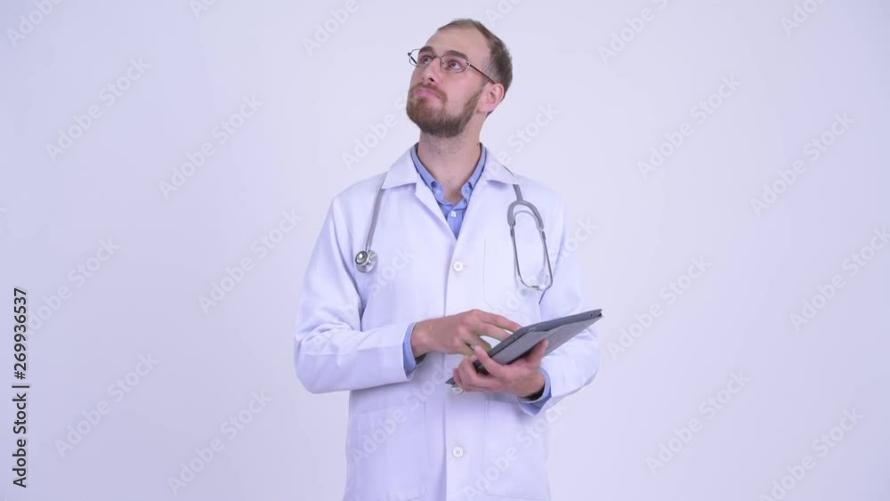 Happy bearded man doctor thinking while using digital tablet Happy bearded man doctor thinking while using digital tablet