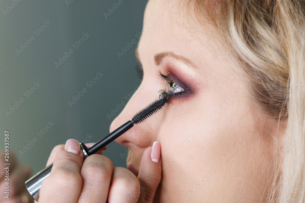 Make-up artist working in make-up studio, applying makeup on face of female clients. Makeup artist applies eye shadow with makeup brush to lower eyelid. Evening make-up.