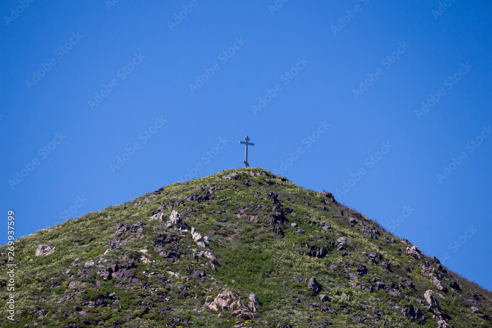 Orthodox cross on the top of a mountain against the background of clear sky.