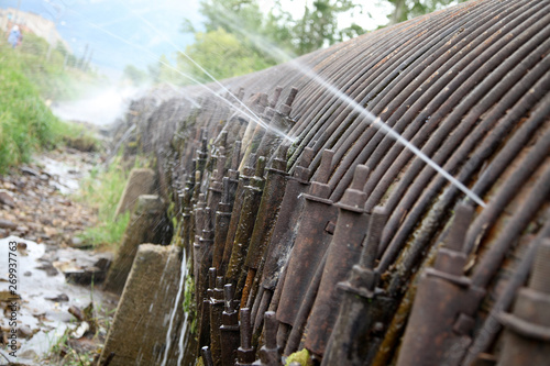 Foto A huge wooden water pipe with old iron straps holding it, as well as with streams of water bursting through places