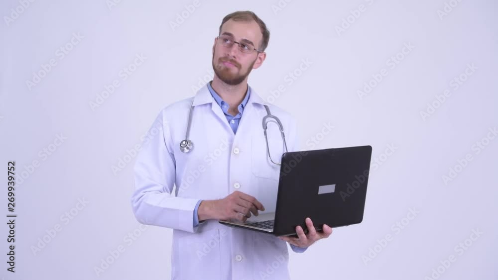 Happy bearded man doctor thinking while using laptop Happy bearded man doctor thinking while using laptop