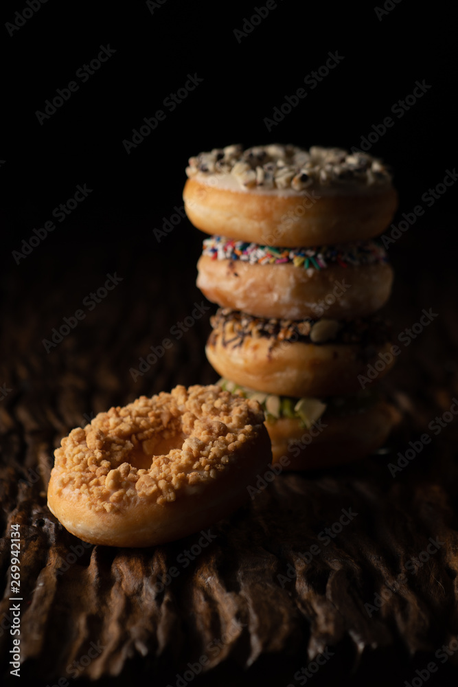 a piece of donut on wooden plank with a stack of donuts behind on dark background a piece of donut on wooden plank with a stack of donuts behind on dark background