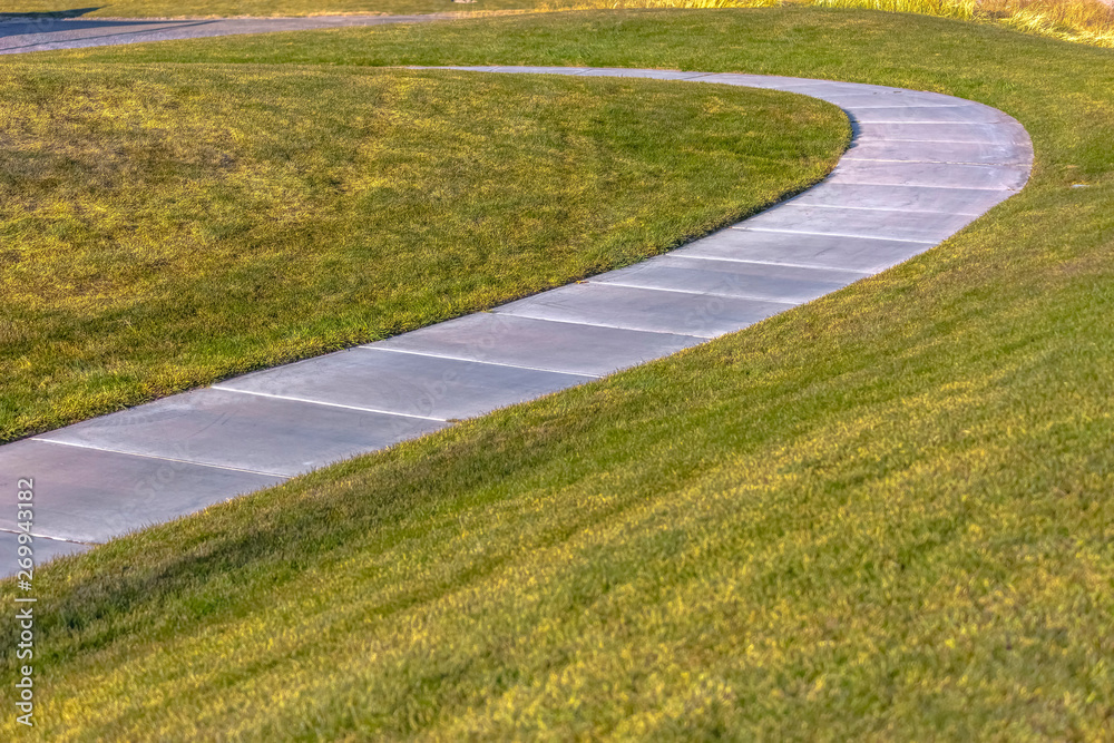 Paved footpath that curves through the grassy terrain viewed on a sunny day