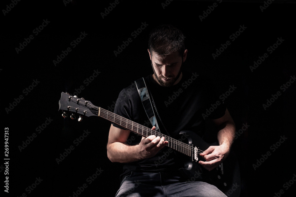one man, playing guitar, dark and moody rock musician. Dark and moody atmosphere and lights. Shot on black background behind.
