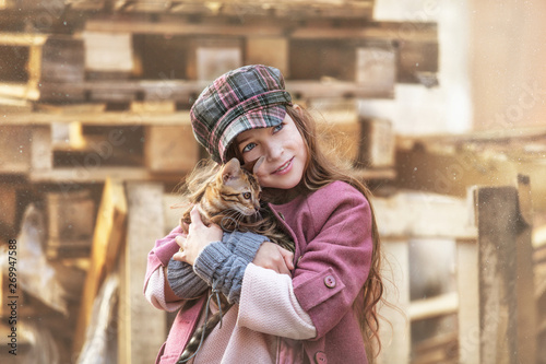 Fashionable child girl beautiful and happy with cute little Bengal kitten together on the street