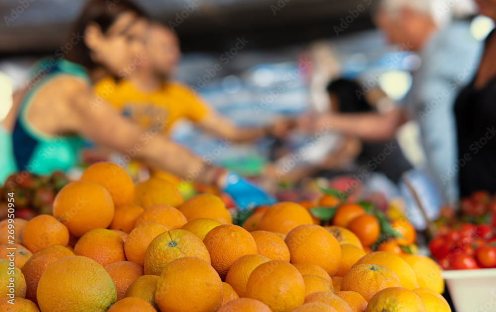 At a market stall at a Spanish weekly market oranges are sold, which are in the foreground. In the background you can see arms and hands of buyers and sellers with nice bokeh.