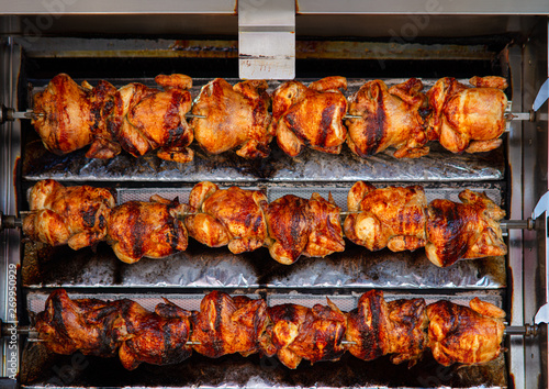 At a stall on a Spanish weekly market, chicken is prepared. They are crispy, fried, and rotate on several skewers on top of each other until they are ready for sale.
