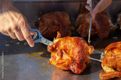 At a stall on a Spanish weekly market, chicken is prepared. The seller takes it from the spit. They are crispy and look delicious.
