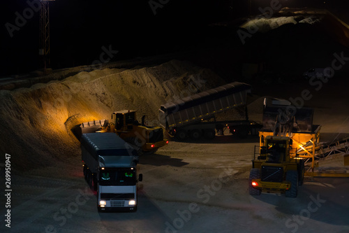 At a southern Spanish port, gypsum is transported by truck at night and loaded onto a cargo ship with wheel loaders. The scenery is illuminated by floodlights.