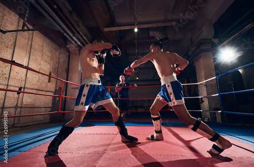 Martial male sportsman kickboxer training kickboxing with sparring partner, fighting in the ring at the sport club