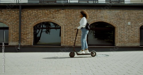 SIDE VIEW Attractive African American black female riding an electric city shared scooter in the street. 4K UHD 60 FPS SLOW MOTION