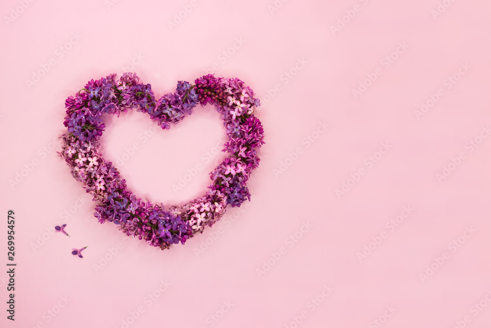Beautiful lilac flowers in shape of heart on pastel pink background. Top view. Copy space.
