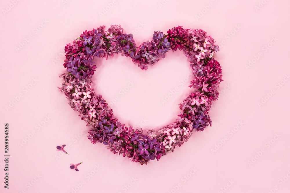 Beautiful lilac flowers in shape of heart on pastel pink background. Top view. Copy space.