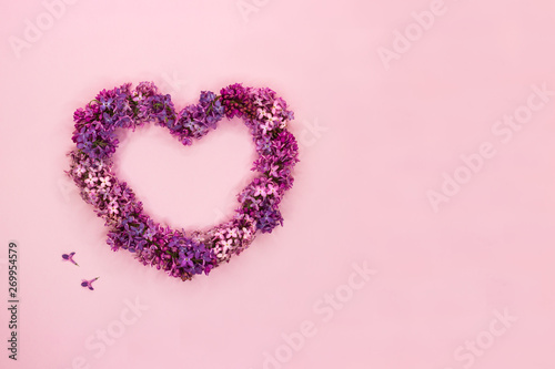 Beautiful lilac flowers in shape of heart on pastel pink background. Top view. Copy space.