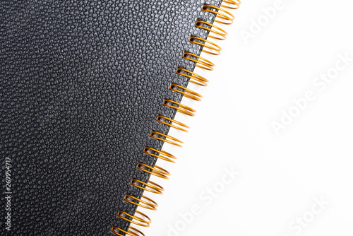An elegant spiral-bound notebook or journal with elegant textured faux leather hard cover artfully set and composed on a plain white background.