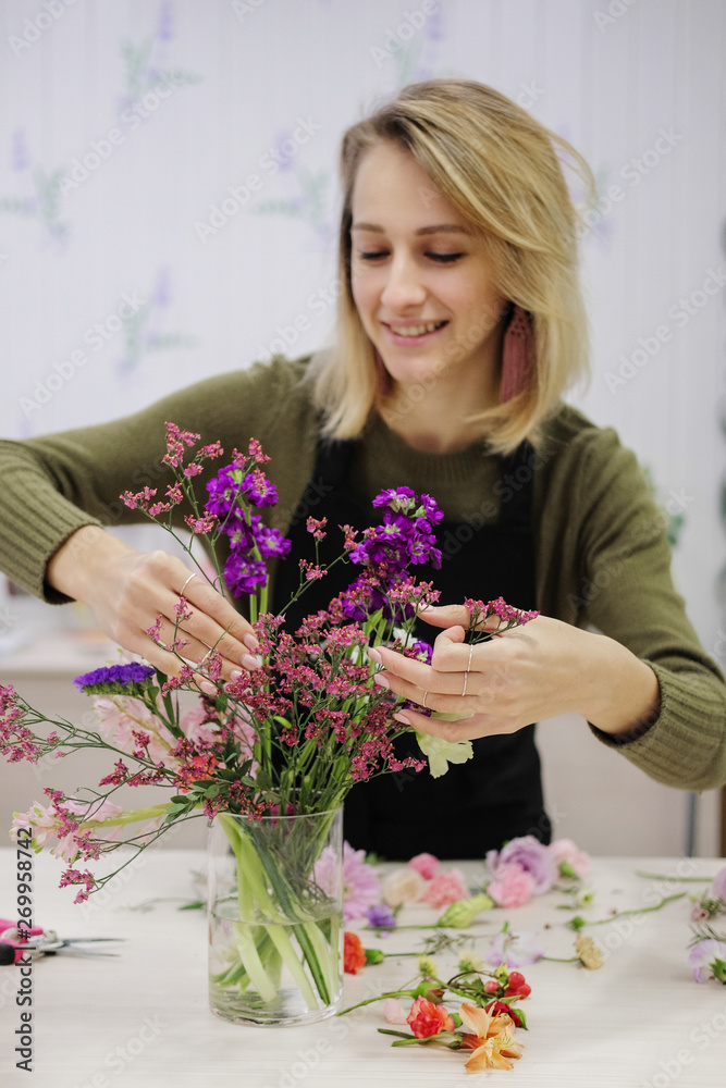 Young female flower seller laughs making up a flower arrangement. Flower shop. A smiling woman cut flowers and puts them in a vase. Young female flower seller laughs making up a flower arrangement. Flower shop. A smiling woman cut flowers and puts them in a vase.