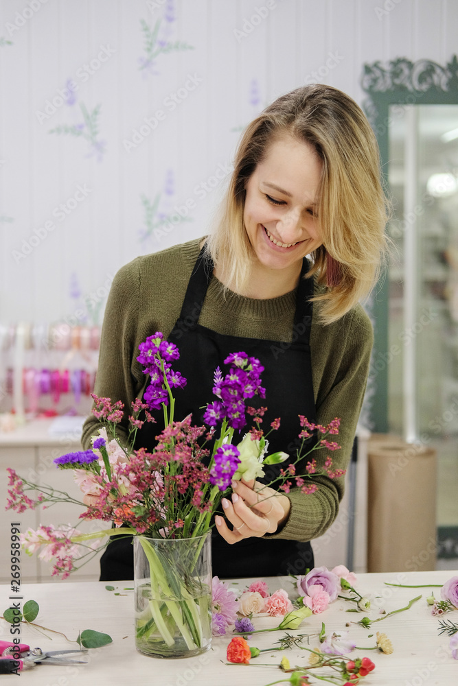 Young female flower seller laughs making up a flower arrangement. Flower shop. A smiling woman cut flowers and puts them in a vase.