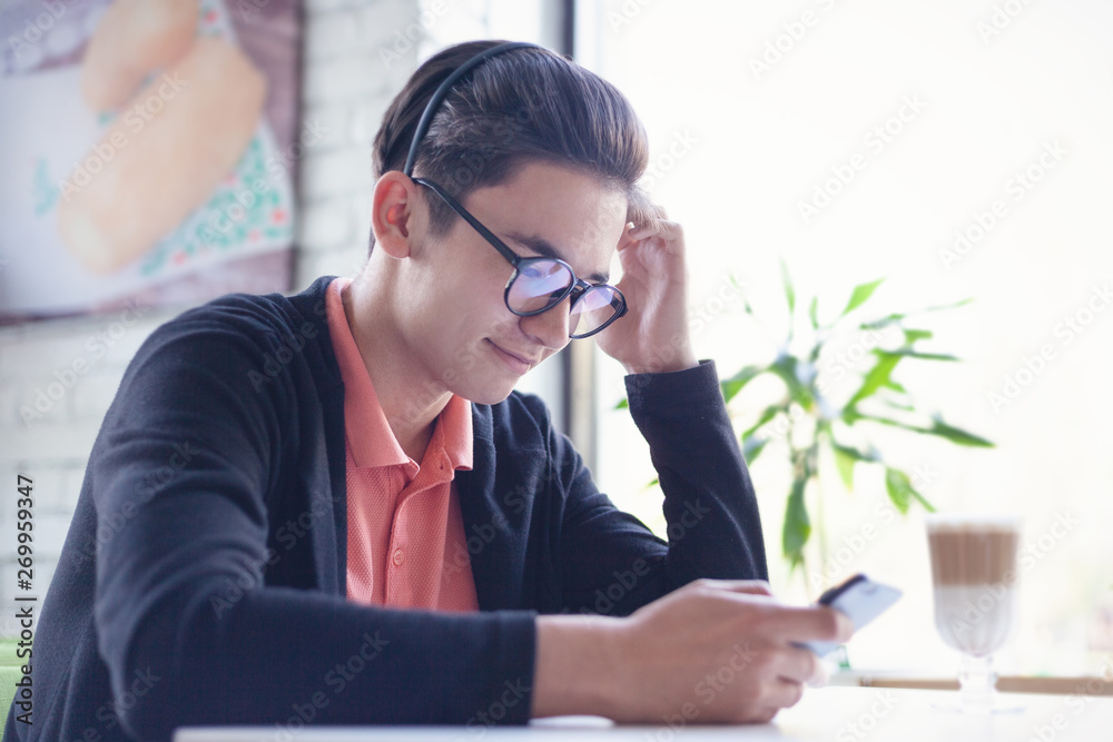Cute Asian teenager in glasses 15-16 years old sits with a phone in a cafe, online education Cute Asian teenager in glasses 15-16 years old sits with a phone in a cafe, online education