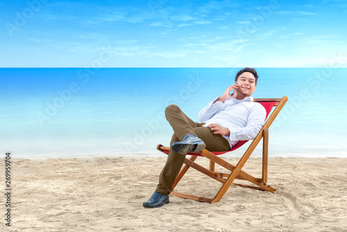 Asian businessman talking on mobile phone while lean back in the beach chair on beach