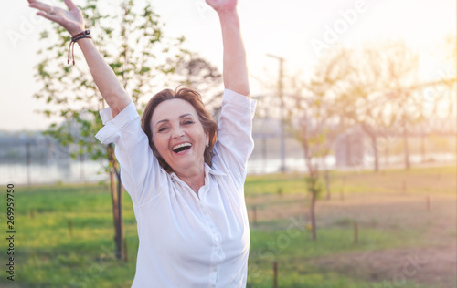 Beautiful happy mature senior smiling elderly woman raises hand up, summer holiday concept