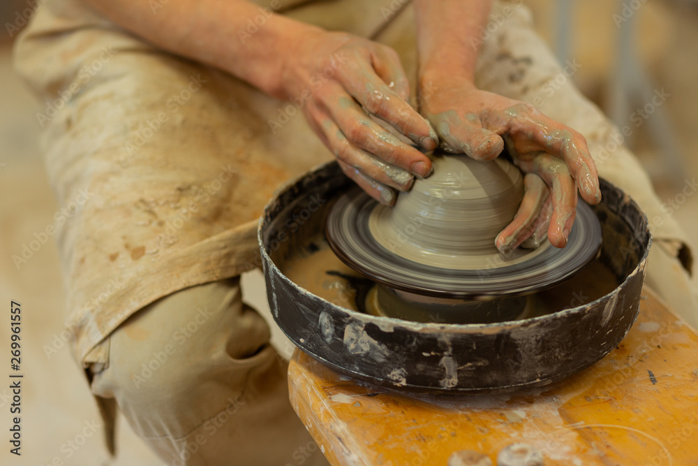 Strong man with dirty hands sitting on wooden pottery wheel Strong man with dirty hands sitting on wooden pottery wheel