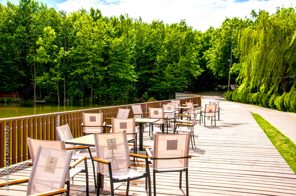 wooden bridge with a fence on which tables and chairs are located. Summer cafe. It's summer outside. The sun is shining. On the background of green forest