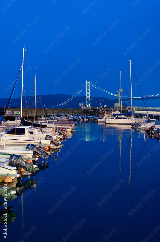 青い夕暮れとライトアップされた明石海峡の橋とヨット